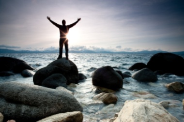 Man standing on a rock, reaching to the sky